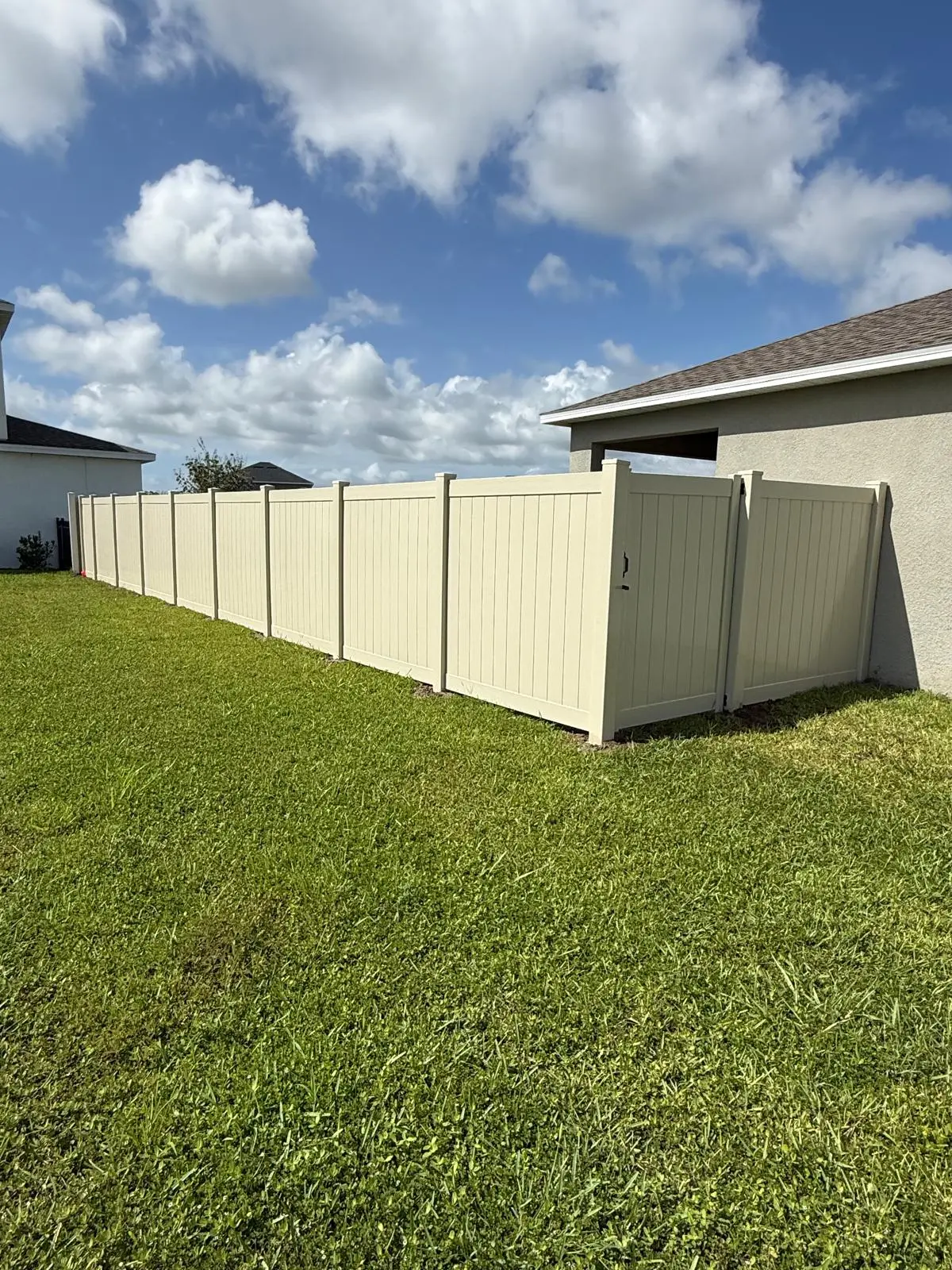 Tan vinyl privacy fence and gate installed along a Tampa, FL backyard